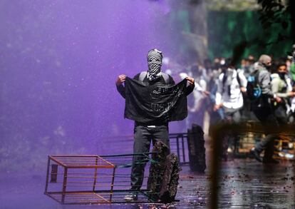 Un estudiante de Cachemira sujeta una bandera negra mientras la policía india usa agua de color para dispersar a los activistas, en Srinagar (India).