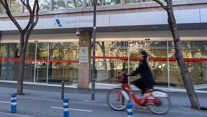 Una mujer pasa en bicicleta frente a una oficina de la Agencia Tributaria.