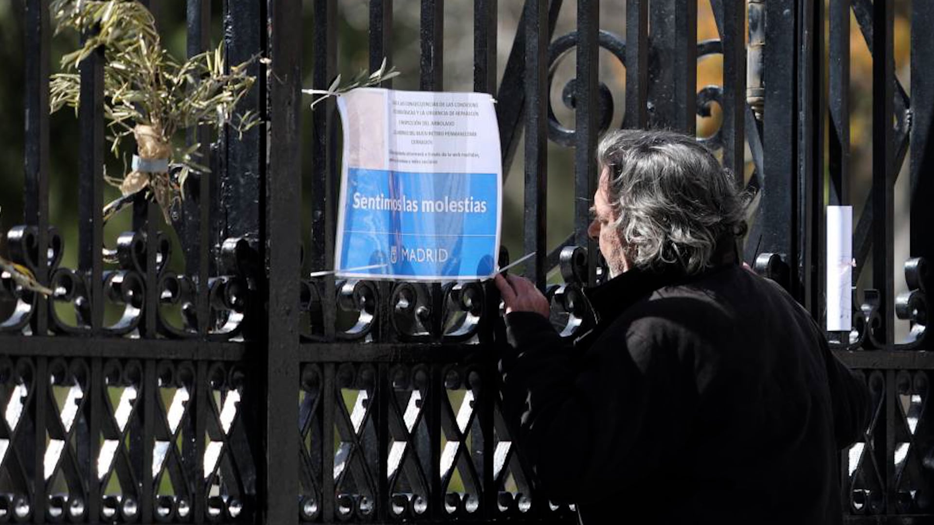 Un mujer mira un cartel que anuncia el cierre temporal del parque del Retiro en la puerta de Reina Mercedes a julio de 2025.