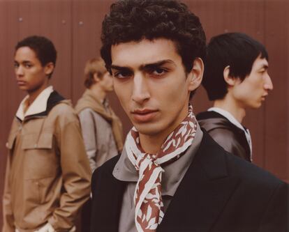 En primer plano, traje negro de lana y mohair, camisa amplia de popelín y ‘carré’ 1000 Feuilles de seda y cachemir. A su derecha, de perfil, el modelo lleva un cortavientos reversible de piel y cachemir. Esta temporada, la gama de colores se centra en los grises, beis, blancos y negros, en un regreso a la elegante sobriedad de la casa, y que subraya las posibilidades técnicas de las prendas diseñadas por Véronique Nichanian, directora del universo masculino de Hermès desde 1988.