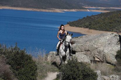 Una joven pasea a caballo por El Berrueco. Al fondo, el embalse de El Atazar.