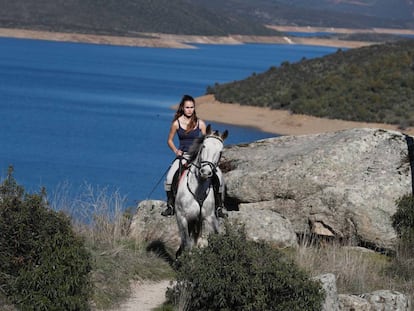 Una joven pasea a caballo por El Berrueco. Al fondo, el embalse de El Atazar.