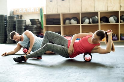 Dos personas hacen ejercicios sobre un rodillo de espuma en un gimnasio.