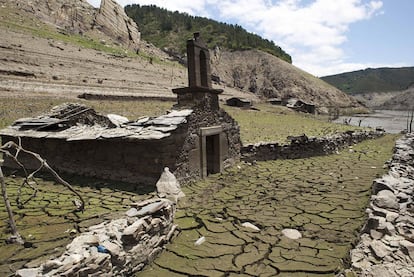 Capilla de Portomeñe, semienterrada en el fango del embalse de Belesar, con algunas construcciones de la aldea al fondo.