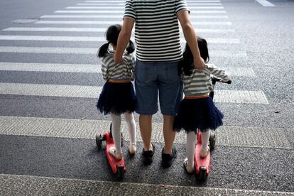 Un padre cruza con sus dos hijas gemelas por un paso de peatones en Shanghai (China), el 28 de septiembre de 2018.