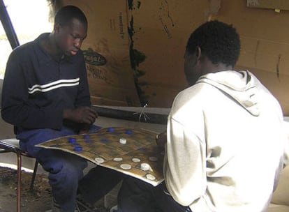 Dos jóvenes de Malí juegan a las damas en el campamento en el que viven, junto a una plantación agrícola de Lepe (Huelva).
