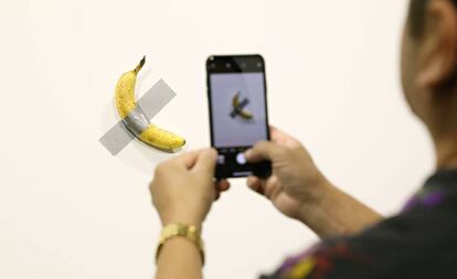 Un visitante saca una foto del plátano adherido a la pared, del artista Maurizio Cattelan.