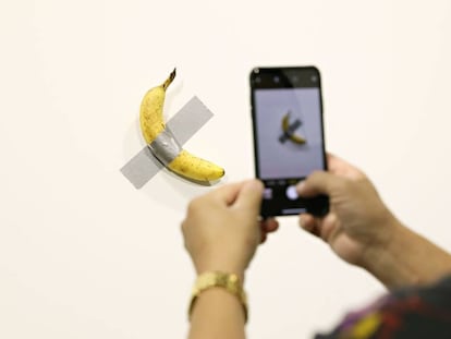 Un visitante saca una foto del plátano adherido a la pared, del artista Maurizio Cattelan.