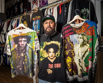 Andrés Muñoz sostiene camisetas de segunda mano de bandas de música que se venden en su tienda de ropa 'vintage' Back of the Closet de Huntington, Nueva York