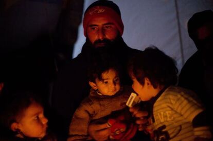 Un hombre se calienta junto a sus hijos en un campo de desplazados de la ciudad siria de Azaz, en el norte de la provincia de Alepo.
