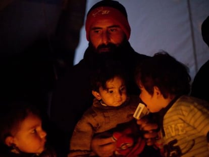 Un hombre se calienta junto a sus hijos en un campo de desplazados de la ciudad siria de Azaz, en el norte de la provincia de Alepo.