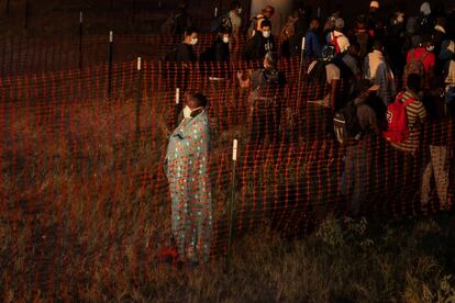 Un migrante, cubierto con una manta, mira hacia un campo que conduce a la frontera con México mientras él y otros esperan subir a un autobús de Aduanas y Protección Fronteriza en Del Rio, Texas.