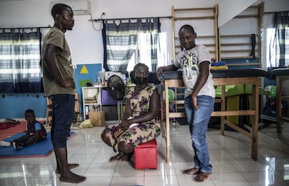 Samiro da Silva, de 15 años (derecha), junto a su madre Santa Aju, de 37, y su terapeuta en el centro de rehabilitación de Aida. "El niño nació normal, pero con nueve empezó a tener problemas. No sabemos si por una meningitis o paludismo cerebral", relata la progenitora. Gracias a la terapia ha recuperado parte de la motricidad. "Quiero poder levantar este brazo y manejar la mano", dice el chico mientras se agarra su izquierda. De hacerlo, podrá atender mejor sus clases en Braille, pues también perdió la visión casi completamente. "Quiero ser médico. Y si no, pastor de la iglesia para contar la palabra de Dios".