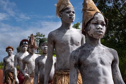 Jovens e crianças, vestidos com roupas contemporâneas misturadas com trajes tradicionais e pintados com pó de mandioca seca, participam de uma cerimônia de educação do governo em Bambari.