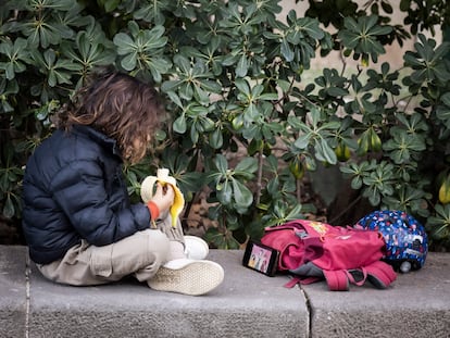 Un niño de primaria mira el móvil mientras desayuna en un parque de Barcelona.