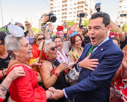 El presidente de la Junta de Andalucía, Juan Manuel Moreno, bromea con un grupo de mujeres vestidas de flamencas, bajo la portada de la Feria de Abril de Sevilla.