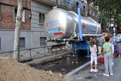 Un grupo de vecinos se acerca a beber hasta el camión cisterna que el Canal de Isabel II llevó hasta la zona.