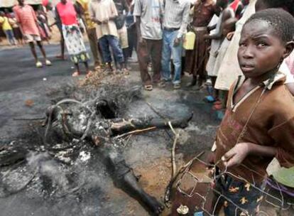 Un niño sujeta su juguete de alambre junto a un cadáver quemado por una turba violenta ayer en Kisumu.