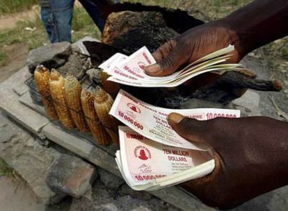 Un hombre maneja fajos de billetes de 10 millones de dólares zimbabuenses en su puesto de venta de maíz en Harare.