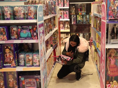 Una mujer observa una muñeca en la sección de juguetes de unos grandes almacenes.