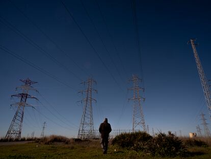 Un hombre pasea cerca de torres de tendido eléctrico a las afueras de Sevilla.