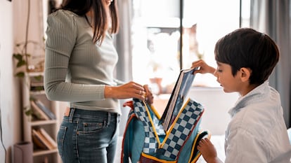 Un niño metiendo libros en la mochila con su madre.