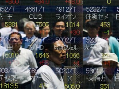 Personas reflejadas en una pantalla con cotizaciones bursátiles, en Tokio (Japón).