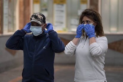 Dos personas se colocan las mascarillas que les han entregado en la estación de autobuses del Prado de San Sebastián de Sevilla.