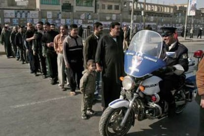 Un policía iraquí atraviesa una fila de votantes ante un colegio electoral en Bagdad.