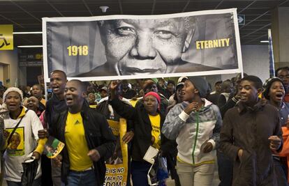 Gente portando una pancarta del presidente Nelson Mandela a la entrada del estadio donde se está celebrando su funeral.