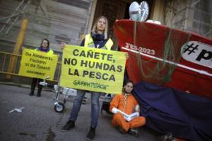 Activistas de Greenpeace durante la protesta que han protagonizado hoy en Madrid en la que han mostrado pancartas con la inscripción "Cañete, no hundas la pesca" y se han encadenado a un barco pesquero colocado delante de la puerta principal del Ministerio de Agricultura, Alimentación y Medio Ambiente para denunciar la política pesquera de esta cartera.