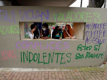 Varias mujeres conversan frente a una pared con grafitis pintados en las paredes de un Comando de Atención Inmediata (CAI) de la Policía durante unas protestas en Bogotá.