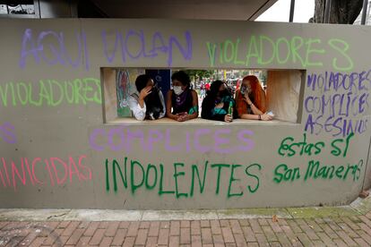 Varias mujeres conversan frente a una pared con grafitis pintados en las paredes de un Comando de Atención Inmediata (CAI) de la Policía durante unas protestas en Bogotá.