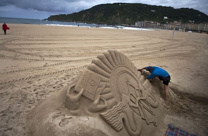 Un hombre realiza una escultura de arena copiando el logotipo del festival en la playa de La Zurriola en San Sebastián.