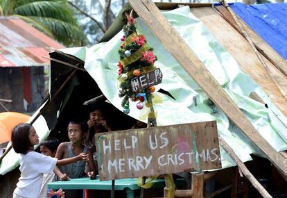 Unos niños filipinos junto a un cartel en el que se puede leer “Ayúdanos, Feliz Navidad” en una calle de Basay en la provincia de Samar, 28 de noviembre de 2013.