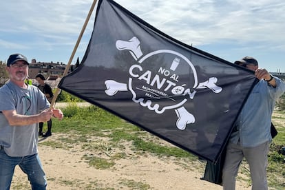 Dos vecinos de Montecarmelo sostienen una bandera de protesta por el cantón frente a la parcela en la que se proyecta, a principios de abril de 2025.