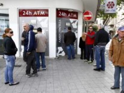Un grupo de personas hace cola junto al cajero autom&aacute;tico de una sucursal cerrada del banco Laiki, en Nicosia.