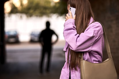 Una mujer habla por teléfono mientras es observada por un hombre en la calle.