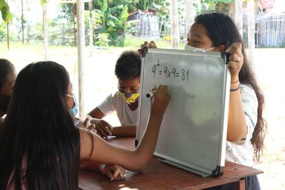 Dennisse Toala tiene 17 años y acaba de terminar Bachillerato. Ella se ha convertido en maestra voluntaria y ha improvisado clases en su barrio, Monte Sinaí, ante las dificultades que presentaban los más pequeños que no tienen recursos para conectarse a aulas virtuales. En la imagen, sostiene la pizarra para que una alumna resuelva una cuenta.