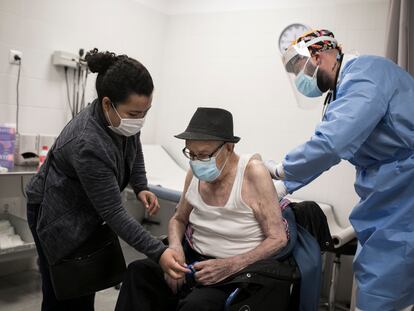 Un paciente, acompañado de su cuidadora, es atendido por un médico en un centro de salud.