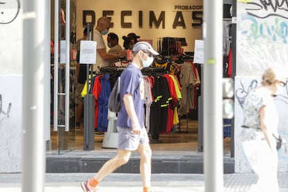 Un hombre protegido con mascarilla pasa junto a una tienda en Madrid.