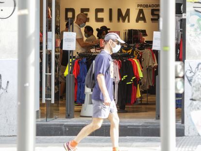 Un hombre protegido con mascarilla pasa junto a una tienda en Madrid.