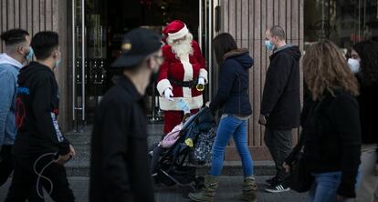 Un Papa Noel llama la atención de los más pequeños en la entrada de un establecimiento comercial en la plaza de Cataluña de Barcelona. En Nochebuena y Nochevieja el toque de queda ordinario, de 22.00 a 6.00, se retrasa a la 1.00, y la víspera del día de Reyes, a las 23.00, en la comunidad catalana.