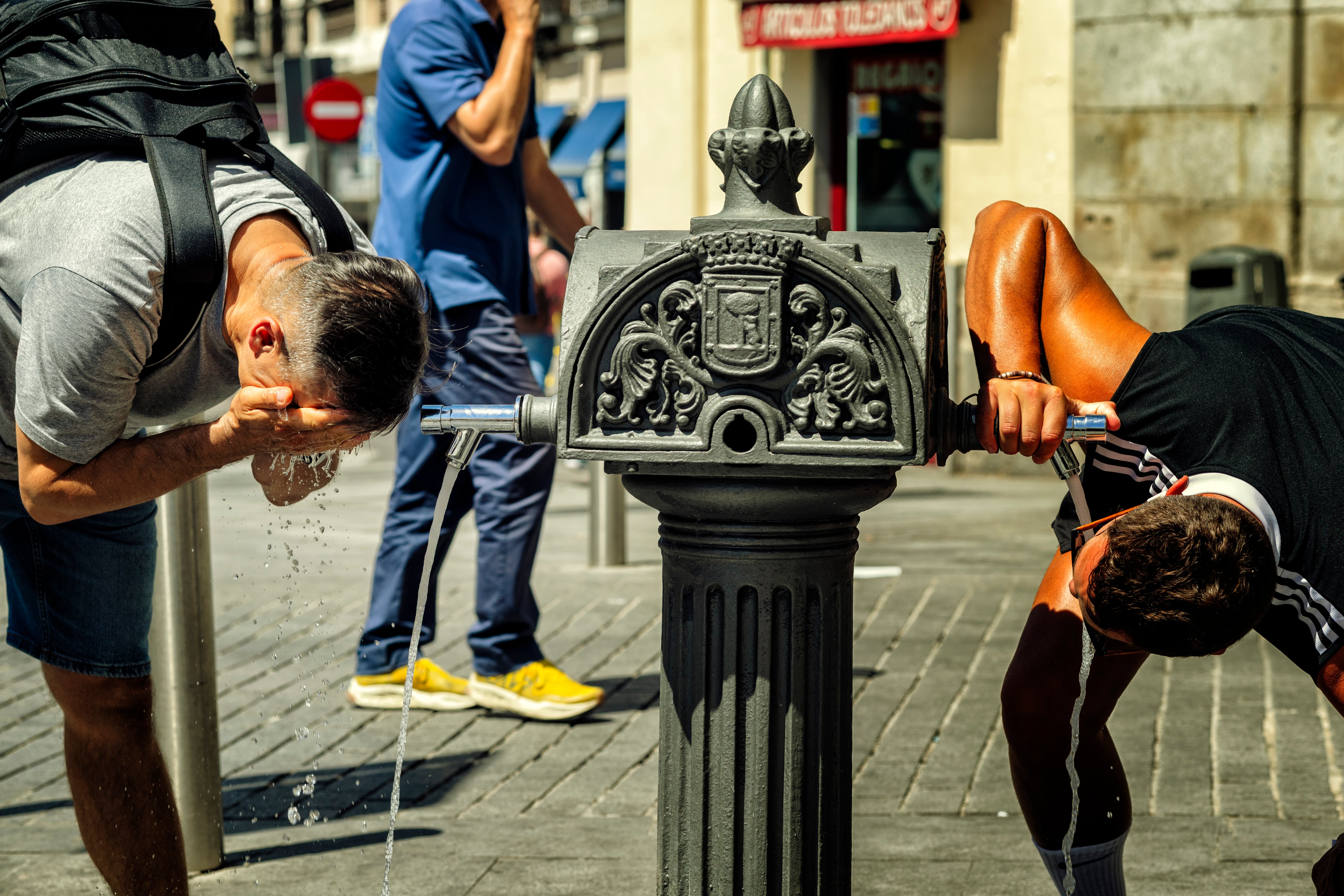 Dos hombres se refrescan en una fuente en el centro de Madrid, este martes.