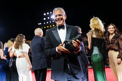 El actor George Clooney sujeta una cámara de fotos durante la alfombra roja.