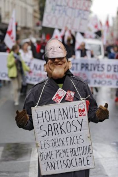 Un hombre con dos caretas, una del presidente francés François Hollande y otra del expresidente francés Nicolás Sarkozy, porta un cartel en el que se lee "Hollande y Sarkozy, las dos caras de una misma política antisocial" durante una manifestación del Primero de Mayo en París, Francia, hoy, jueves 1 de mayo de 2014.