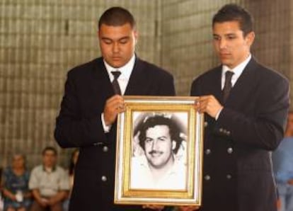 Dos jóvenes no identificados sostienen una fotografía del extinto capo del narcotráfico Pablo Escobar Gaviria durante la misa realizada en el parque cementerio Jardines Montesacro, al sur de Medellín, el 30 de noviembre de 2003 , para conmemorar el décimo aniversario de la muerte de Escobar. EFE/Archivo