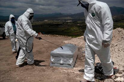 Tres trabajadores desinfectan el ataúd de un fallecido por covid en México.