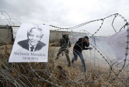 Un cartel que recuerda a Nelson Mandela cuelga de un alambre de púas mientras un manifestante palestino reacciona al gas lacrimógeno disparado por soldados israelíes durante los enfrentamientos tras la manifestación semanal contra los asentamientos judíos en la aldea cisjordana de Bilin, cerca de Ramala.