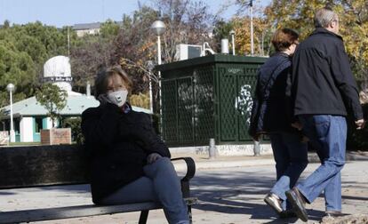 Una mujer sentada en un banco con mascarilla junto a una estación de control de aire, en el Barrio del Pilar.